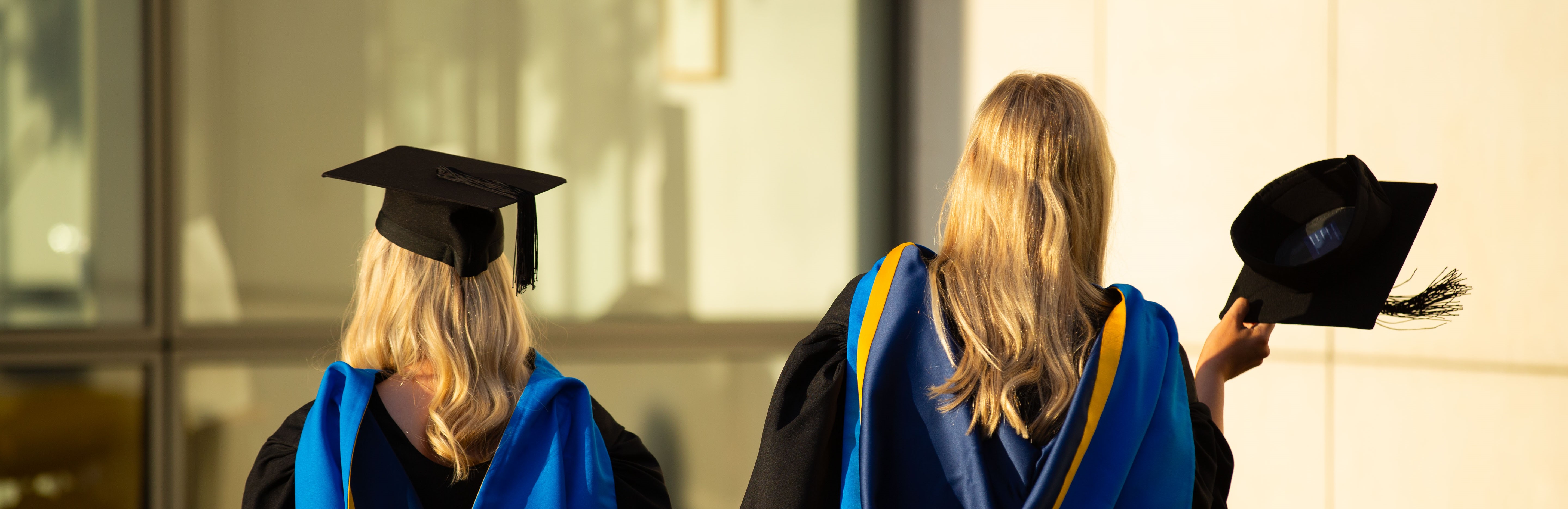 Two blonde graduates photographed from the back wearing UCD graduation robes